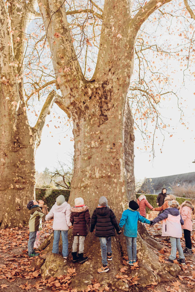 Kinder stehen gemeinsam unter einem Baum auf dem Schulhof